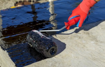 waterproofing coating workers hand in protective gloves applies bitumen mastic on the foundation