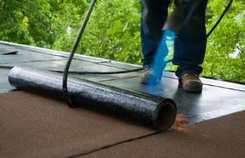 a roofer using a torch to install an elastomeric membrane over a roof