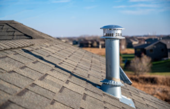 side view of a galvanized metal chimney exhaust on asphalt roof with a rain cap